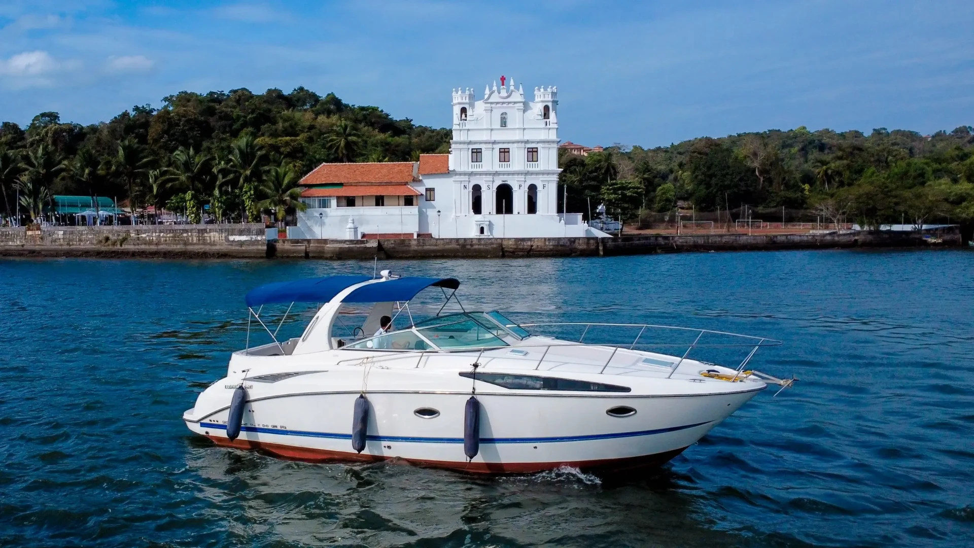 White yacht on the river below a Goa church