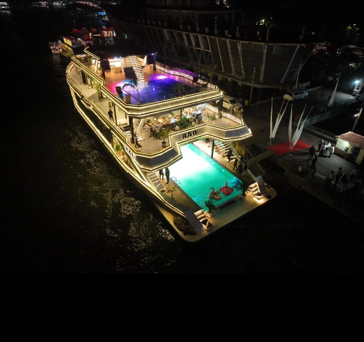 Aerial night view of a cruise boat deck with lounge seating, pool and warm LED lighting