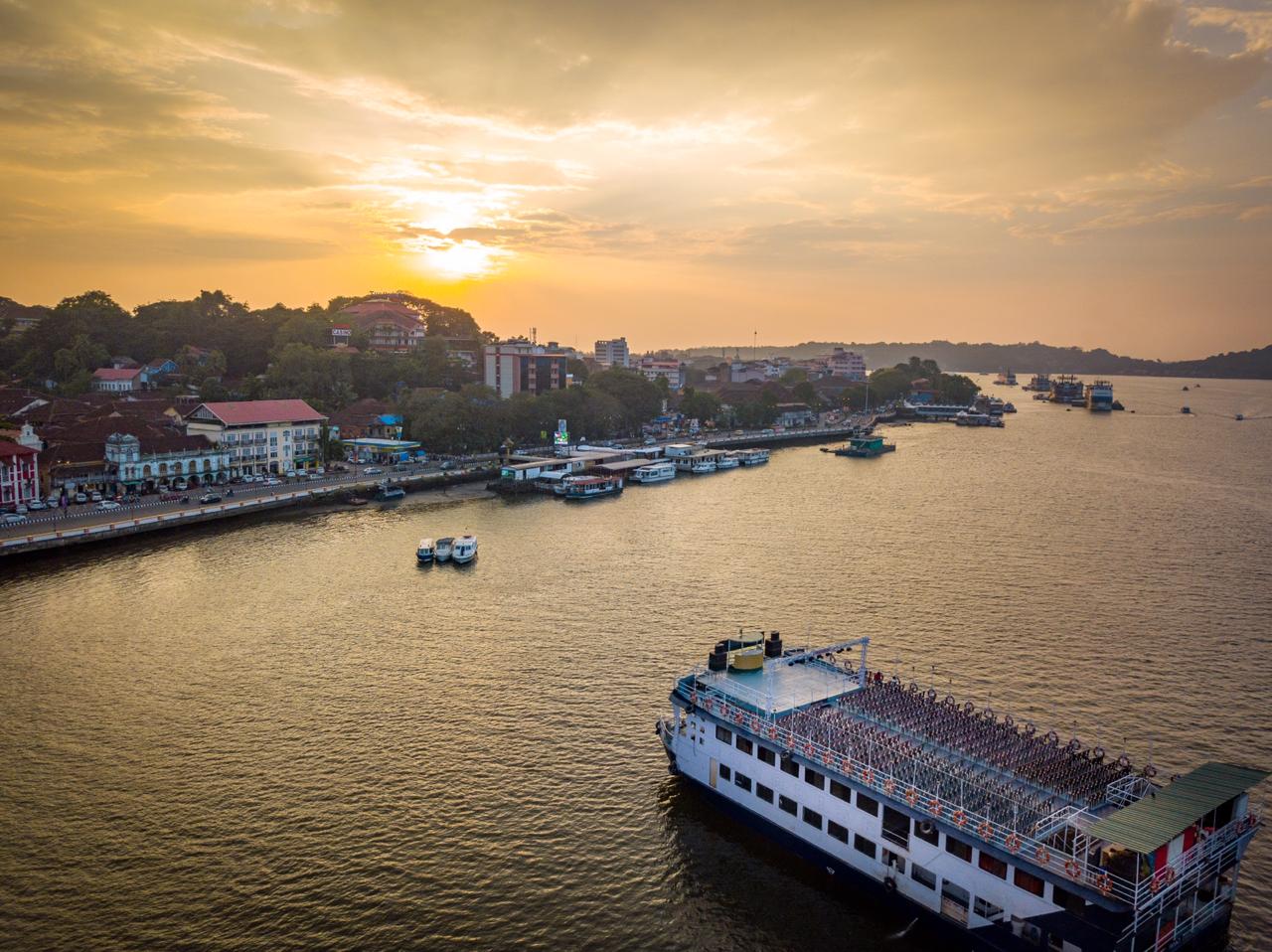 Aerial view of a full Mandovi river cruise boat on the golden-hour water in Panaji, Goa, with sunset light through the clouds