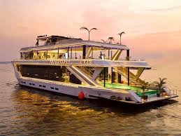 Multi-deck party boat lit up at dusk on the river, with an open sun deck and lounge area aft